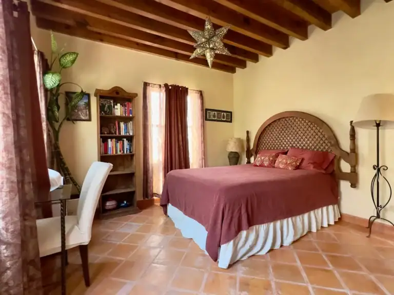 Casa Trebol, bedroom with a lattice-back wood bed, a red bedspread, a bookshelf, a desk and a timber ceiling with a tin star lamp, San Miguel de Allende