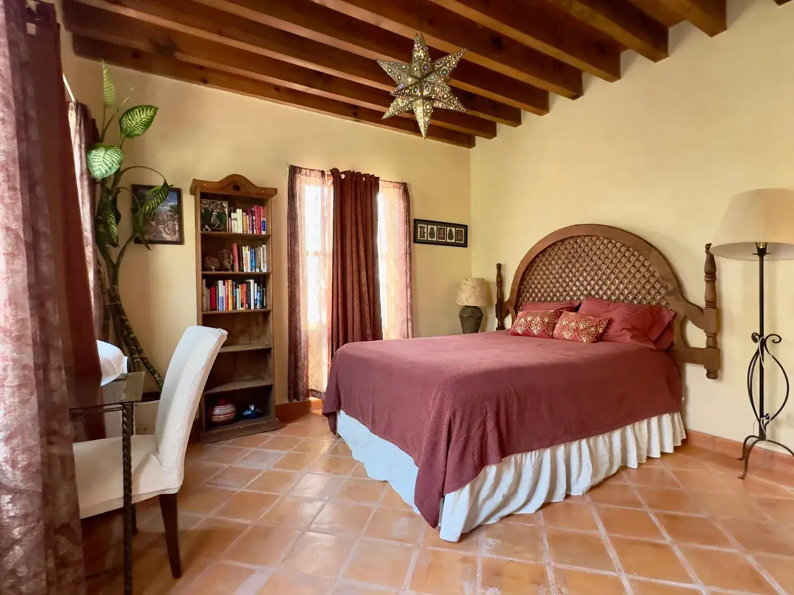 Casa Trebol, bedroom with a lattice-back wood bed, a red bedspread, a bookshelf, a desk and a timber ceiling with a tin star lamp, San Miguel de Allende