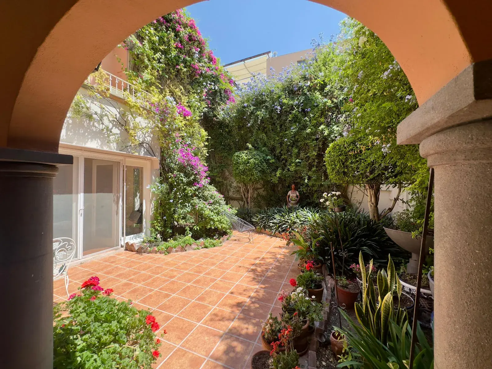 Casa Trebol, view through a stone arch to a garden courtyard with climbing bougainvillea and a glass-walled room, San Miguel de Allende