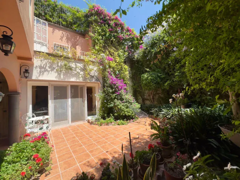 Casa Trebol, garden courtyard with a tile patio, pink bougainvillea climbing the house wall and a glass door room, San Miguel de Allende