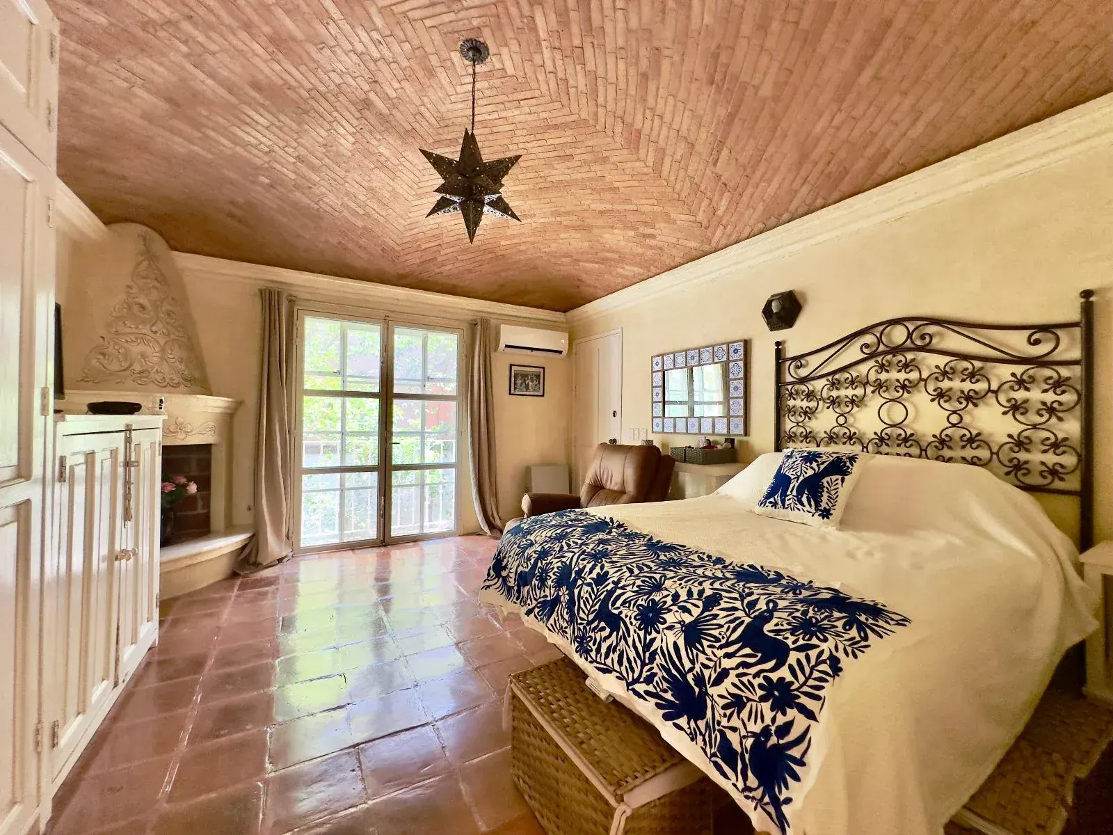 Casa Trebol, bedroom with a wrought-iron headboard, a navy and cream embroidered bedspread, a brick vaulted ceiling and a corner fireplace, San Miguel de Allende