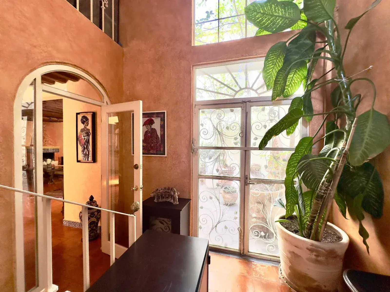 Casa Trebol, double-height room with a tall plant, an arched doorway and French doors with iron grilles, San Miguel de Allende