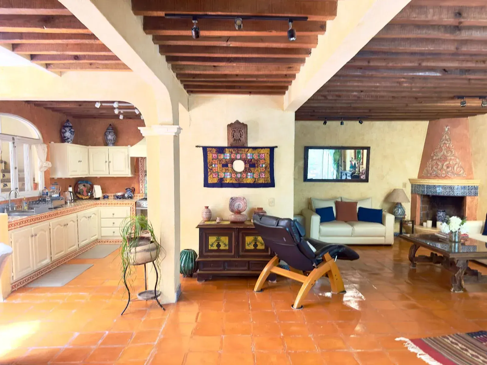Casa Trebol, open living area with a fireplace, white sofas, a recliner and a kitchen with arches beyond, San Miguel de Allende
