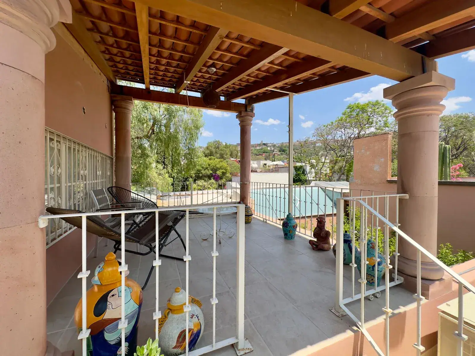 Casa Trebol, covered balcony with stone columns, a pergola, a lounge chair and a view of trees, San Miguel de Allende