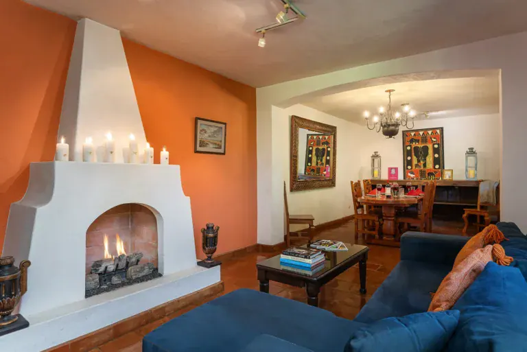 Casa Victoria, living room with a corner fireplace and an orange accent wall, San Miguel de Allende
