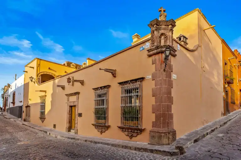 Casa White Magnolias, corner facade of the peach-colored colonial house with barred windows and a stone corner column, San Miguel de Allende