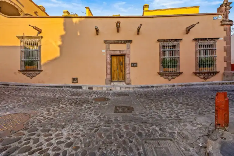 Casa White Magnolias, street facade with a wooden door and three barred windows on a cobblestone street, San Miguel de Allende