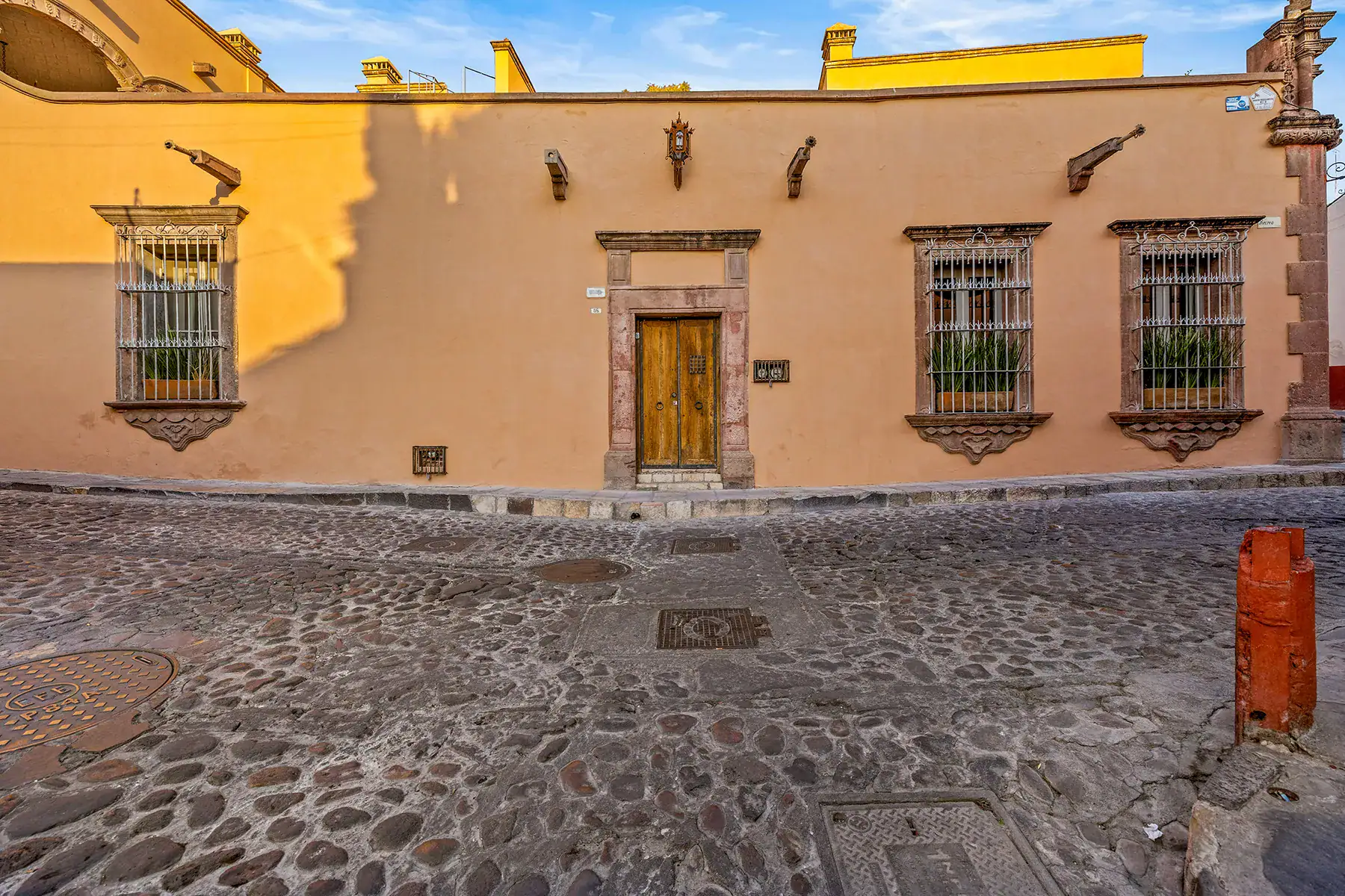 Casa White Magnolias, street facade with a wooden door and three barred windows on a cobblestone street, San Miguel de Allende