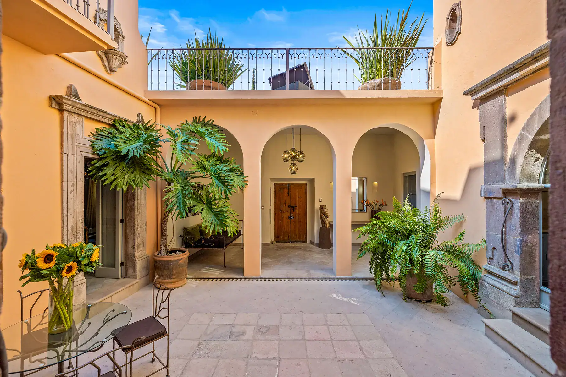 Casa White Magnolias, two-story courtyard with arched doorways, tropical plants and a balcony terrace above, San Miguel de Allende