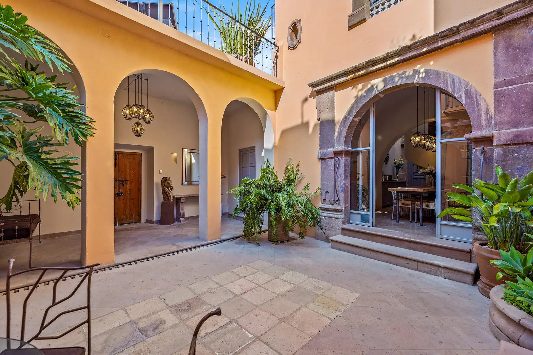 Casa White Magnolias, courtyard with arched entries, a stone-framed glass doorway and a monstera plant, San Miguel de Allende