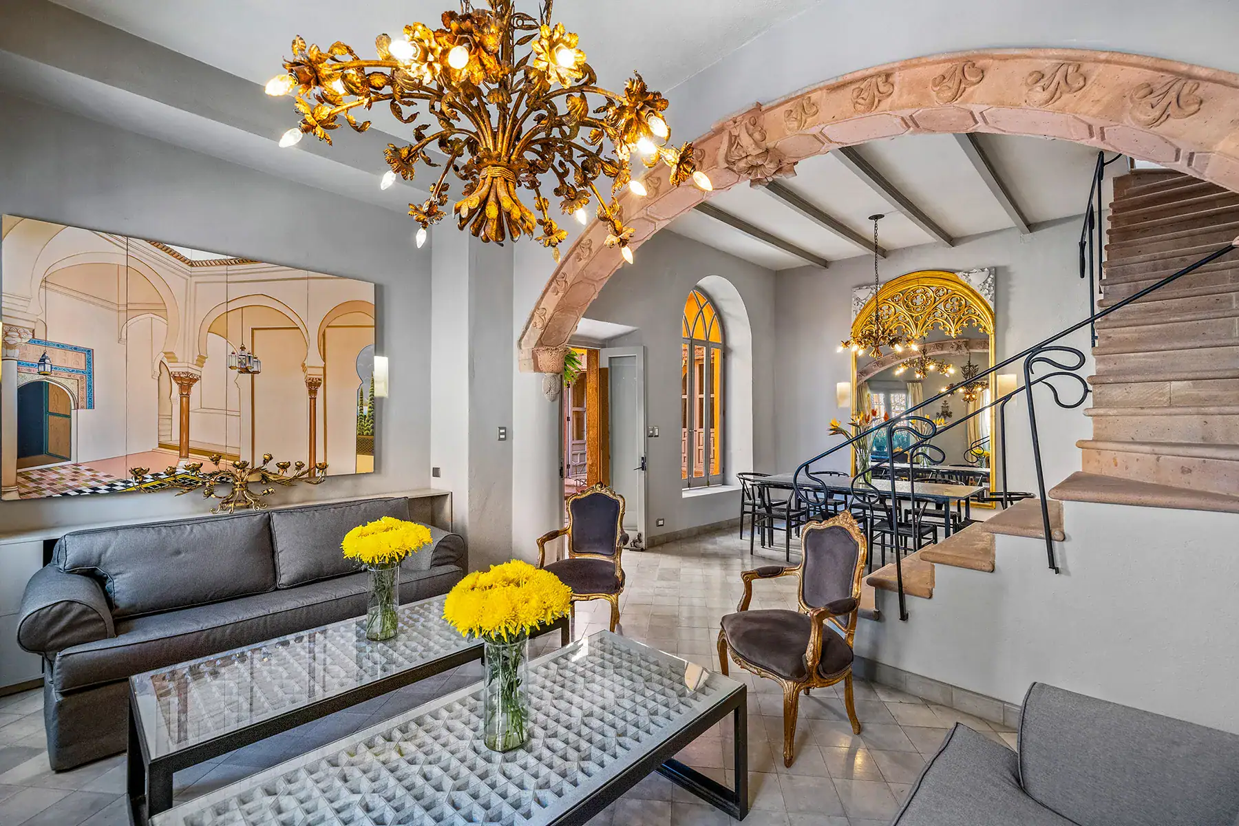 Casa White Magnolias, living area with a leather sofa, glass coffee table, gold chandelier and a stone arch over the stairs, San Miguel de Allende