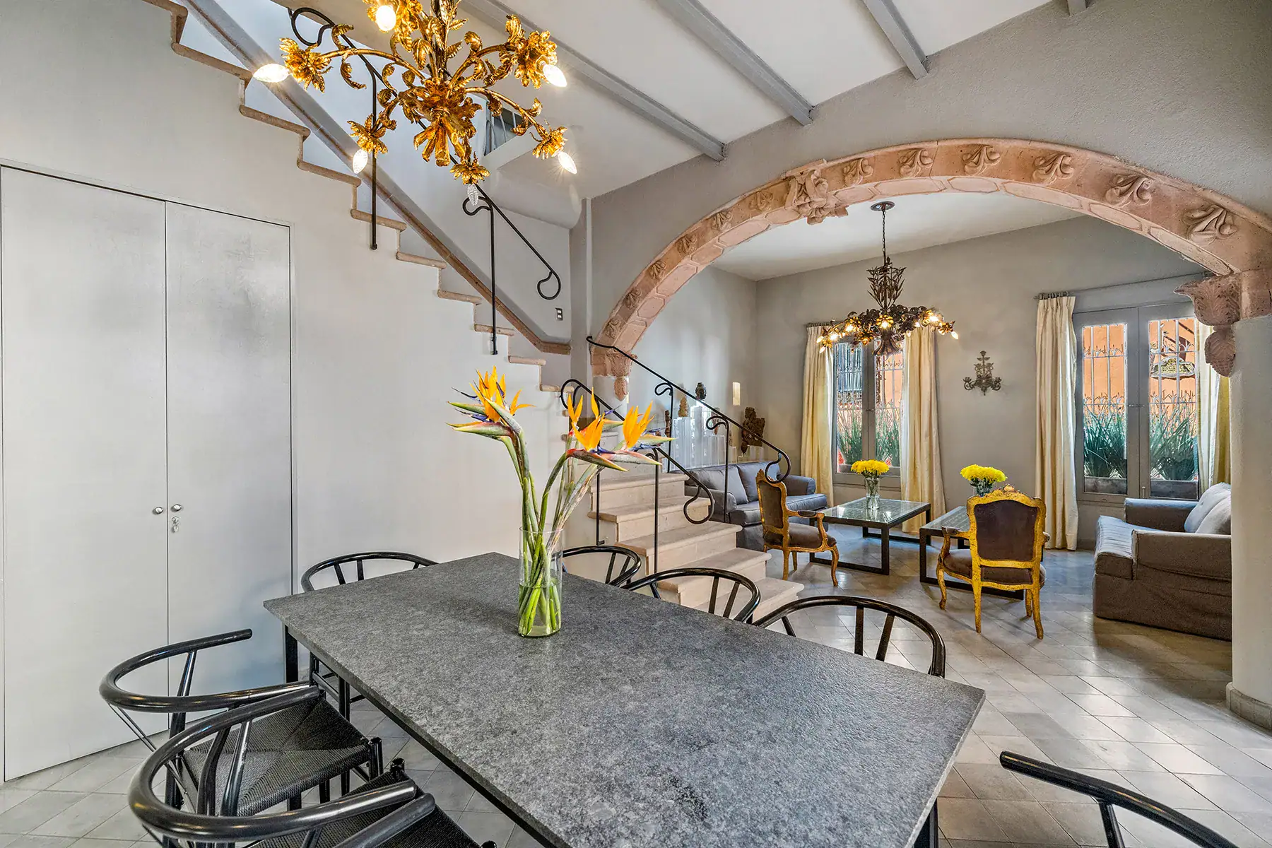 Casa White Magnolias, dining table and stone staircase beneath a gold chandelier, San Miguel de Allende