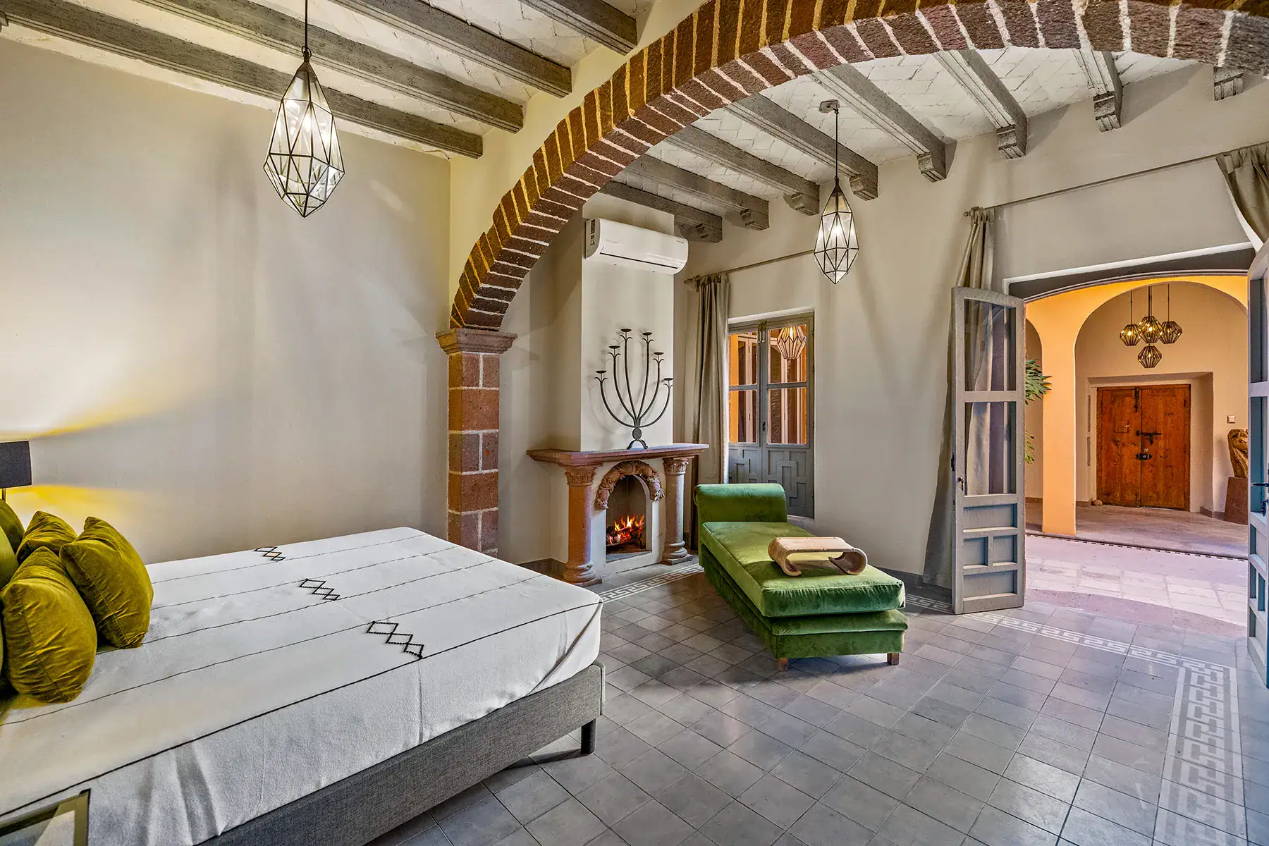 Casa White Magnolias, bedroom with a brick arch, green chaise, corner fireplace and a candelabra wall sculpture, San Miguel de Allende
