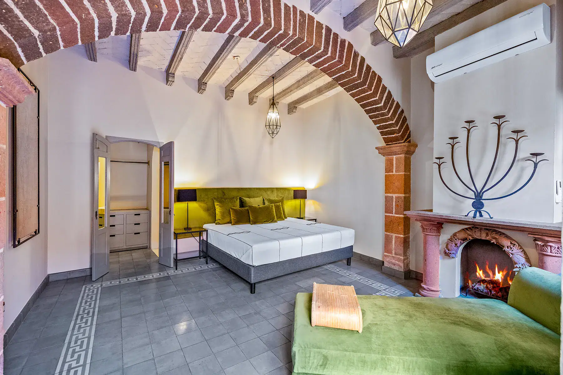 Casa White Magnolias, bedroom with a brick arch, fireplace and green chaise under beamed ceilings, San Miguel de Allende