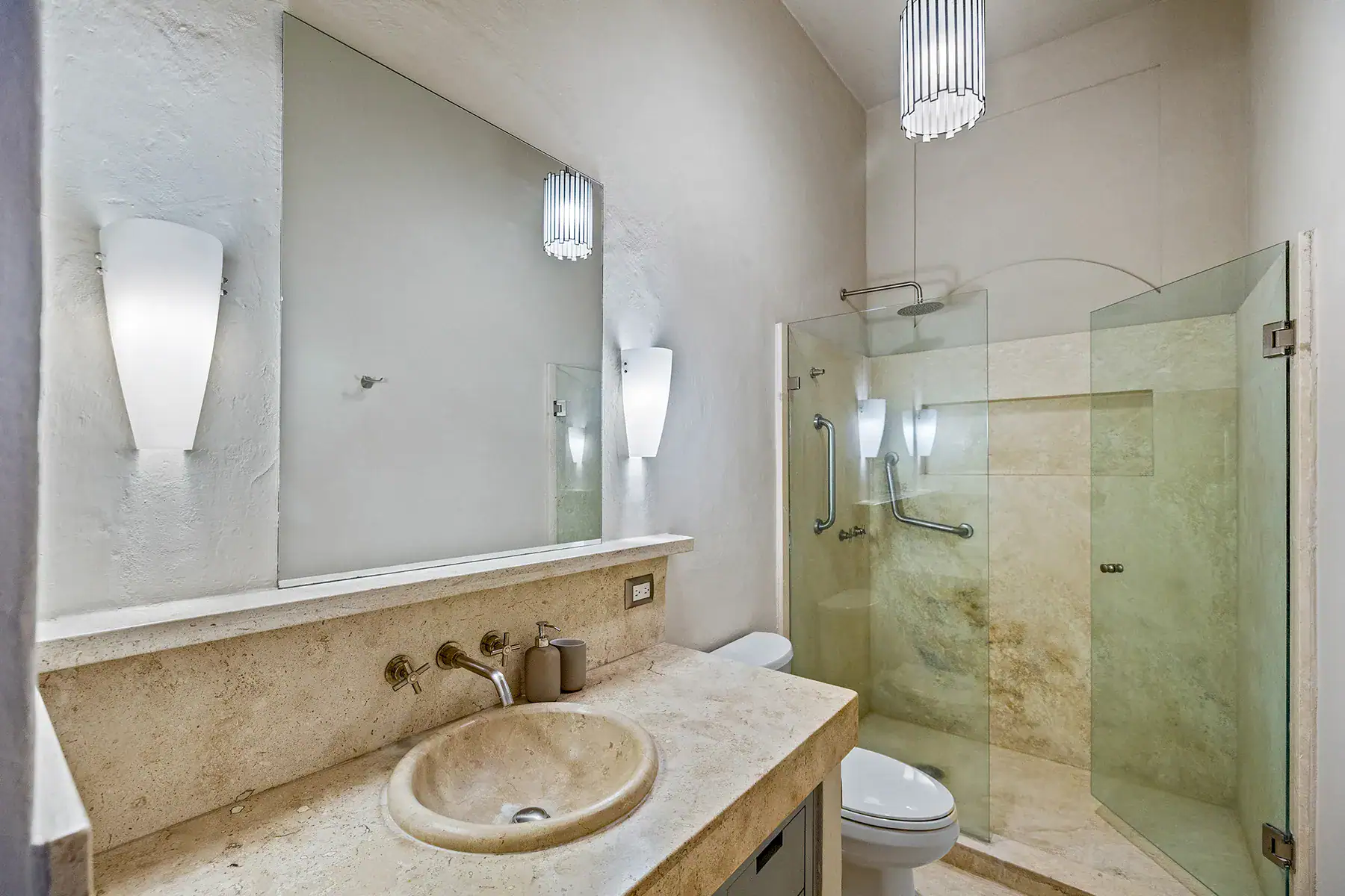 Casa White Magnolias, bathroom with a travertine vanity, stone sink and a glass shower, San Miguel de Allende