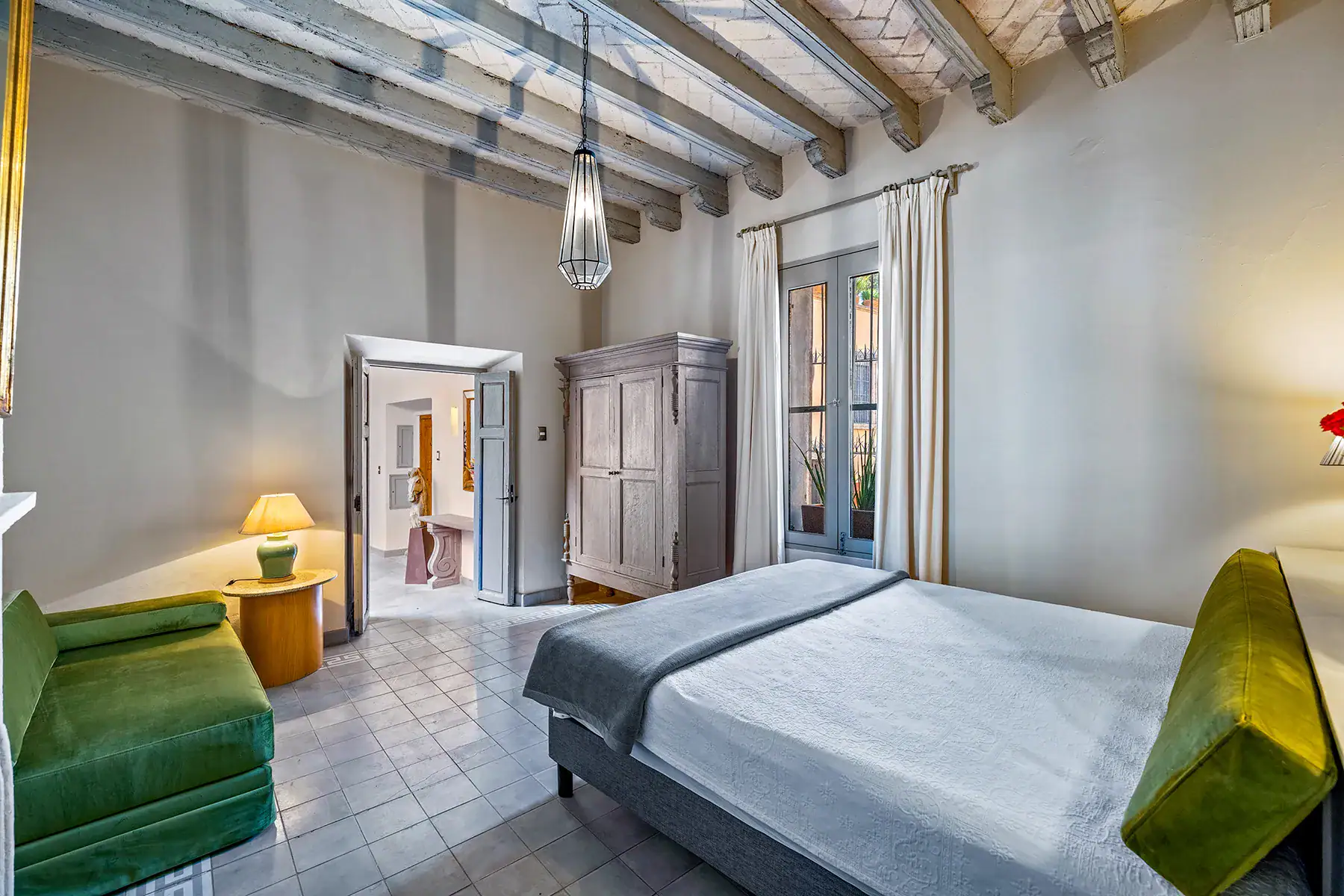 Casa White Magnolias, bedroom with a gray bed, green chair and French doors beneath a beamed ceiling, San Miguel de Allende