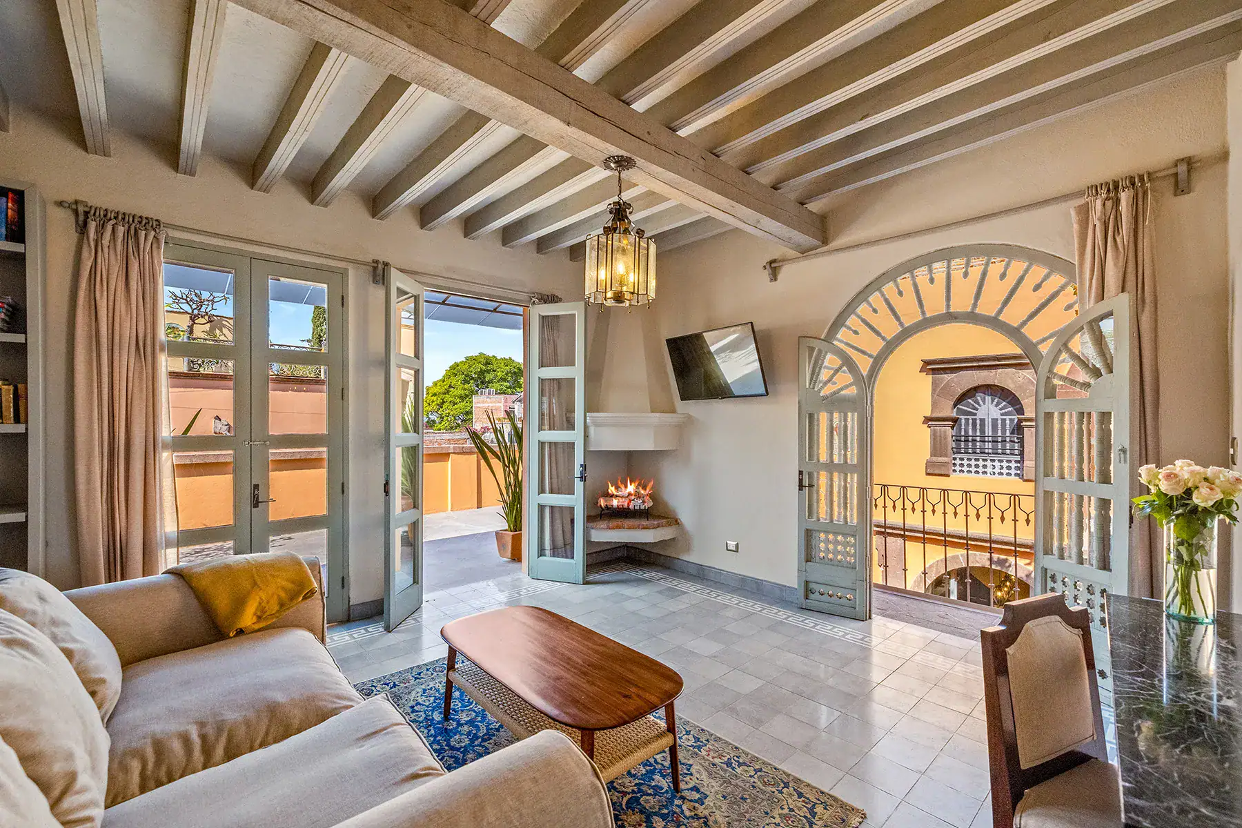 Casa White Magnolias, living room with beige sofas, a wood coffee table and an arched window opening to the terrace, San Miguel de Allende