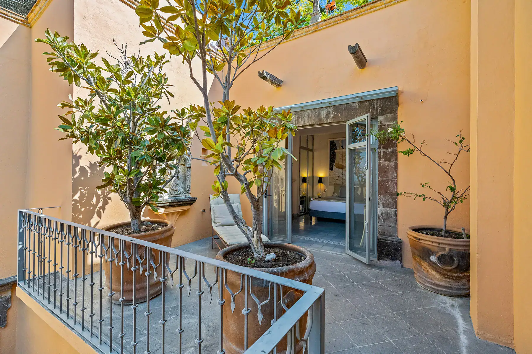 Casa White Magnolias, balcony courtyard with potted citrus trees, an iron railing and a view into a bedroom, San Miguel de Allende