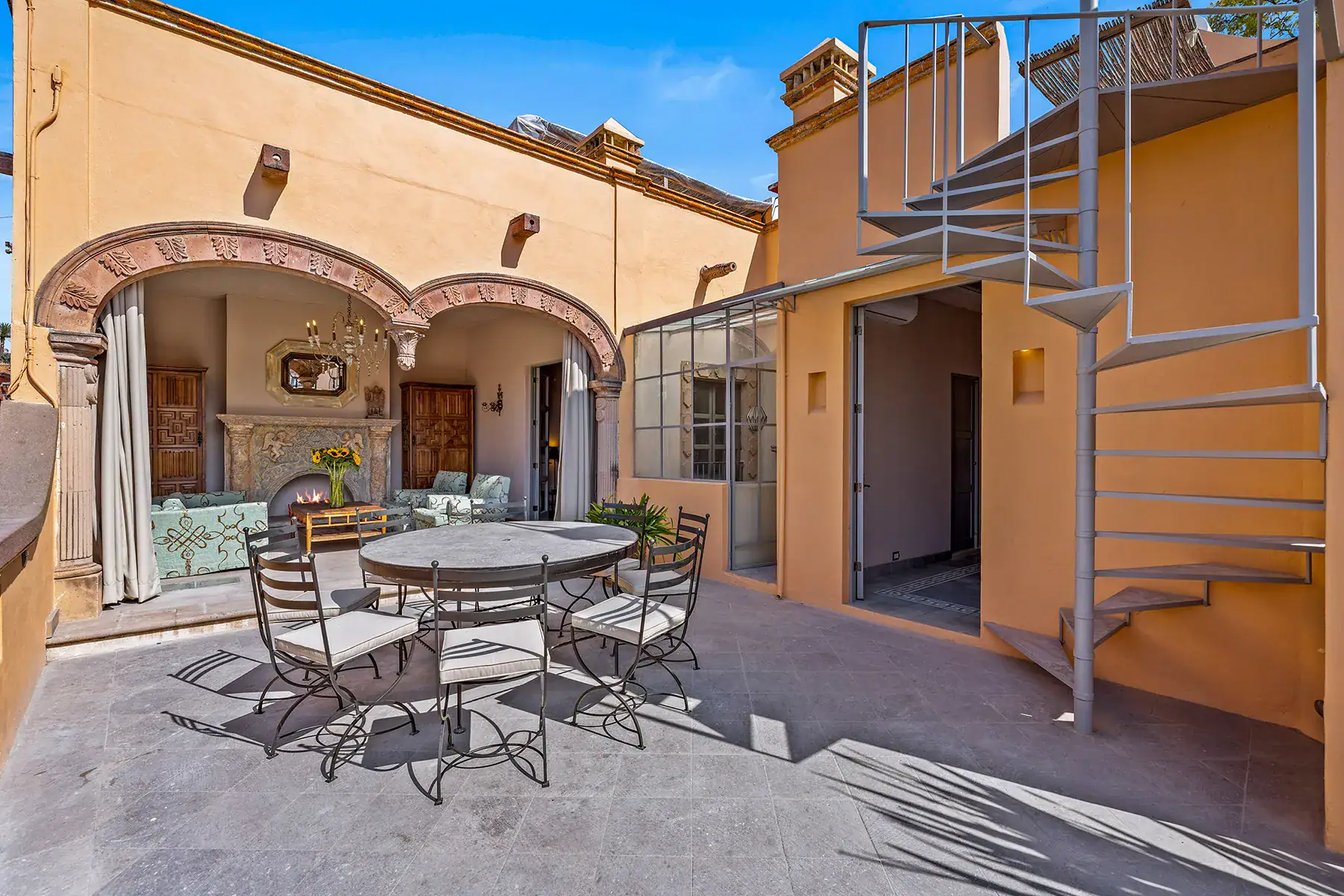 Casa White Magnolias, terrace with a round dining table and a spiral staircase beside a stone arcade, San Miguel de Allende