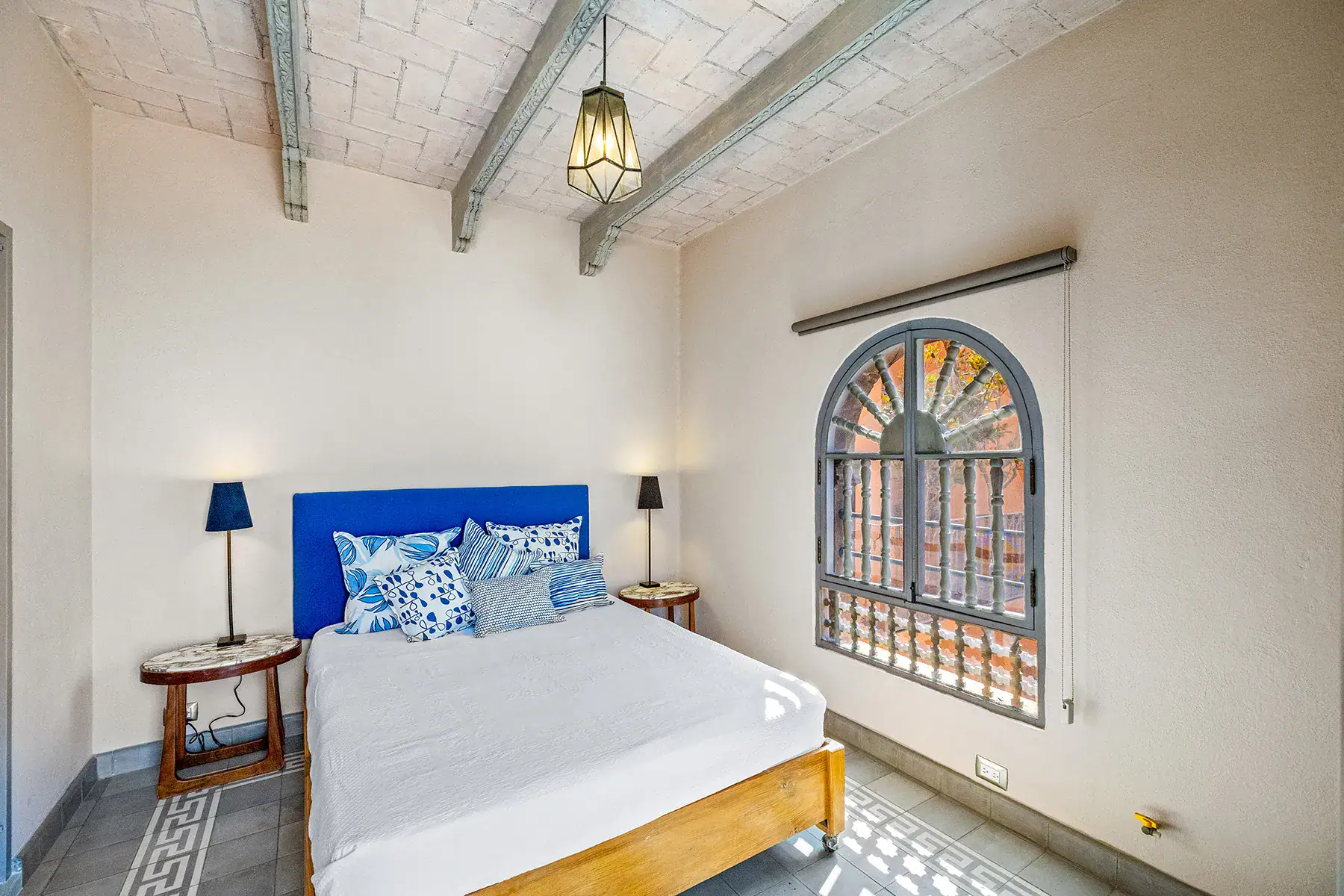 Casa White Magnolias, bedroom with a blue headboard, an arched grille window and a patterned floor, San Miguel de Allende