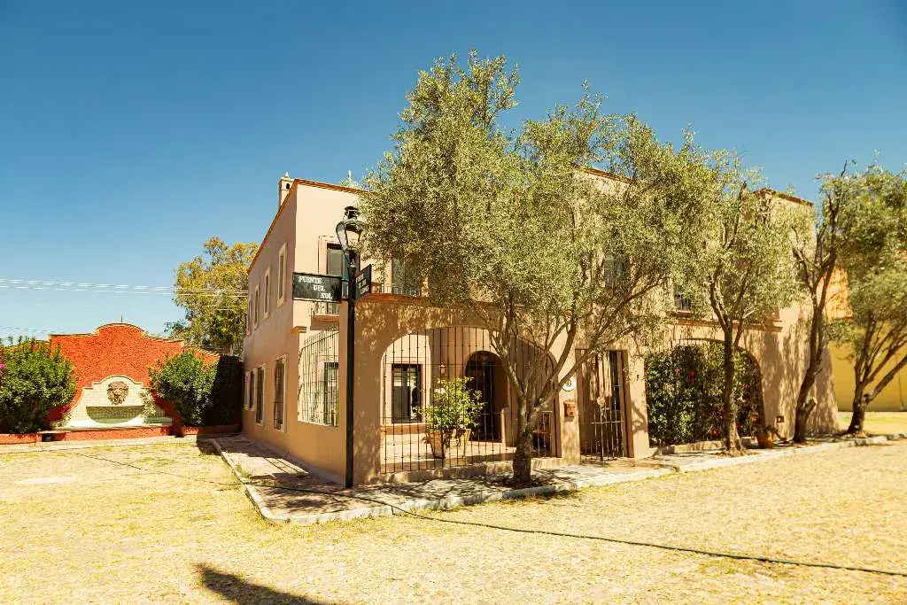 Casa Winston, peach two-story house with an arcade and a lamp post behind olive trees on a dry gravel lot, San Miguel de Allende