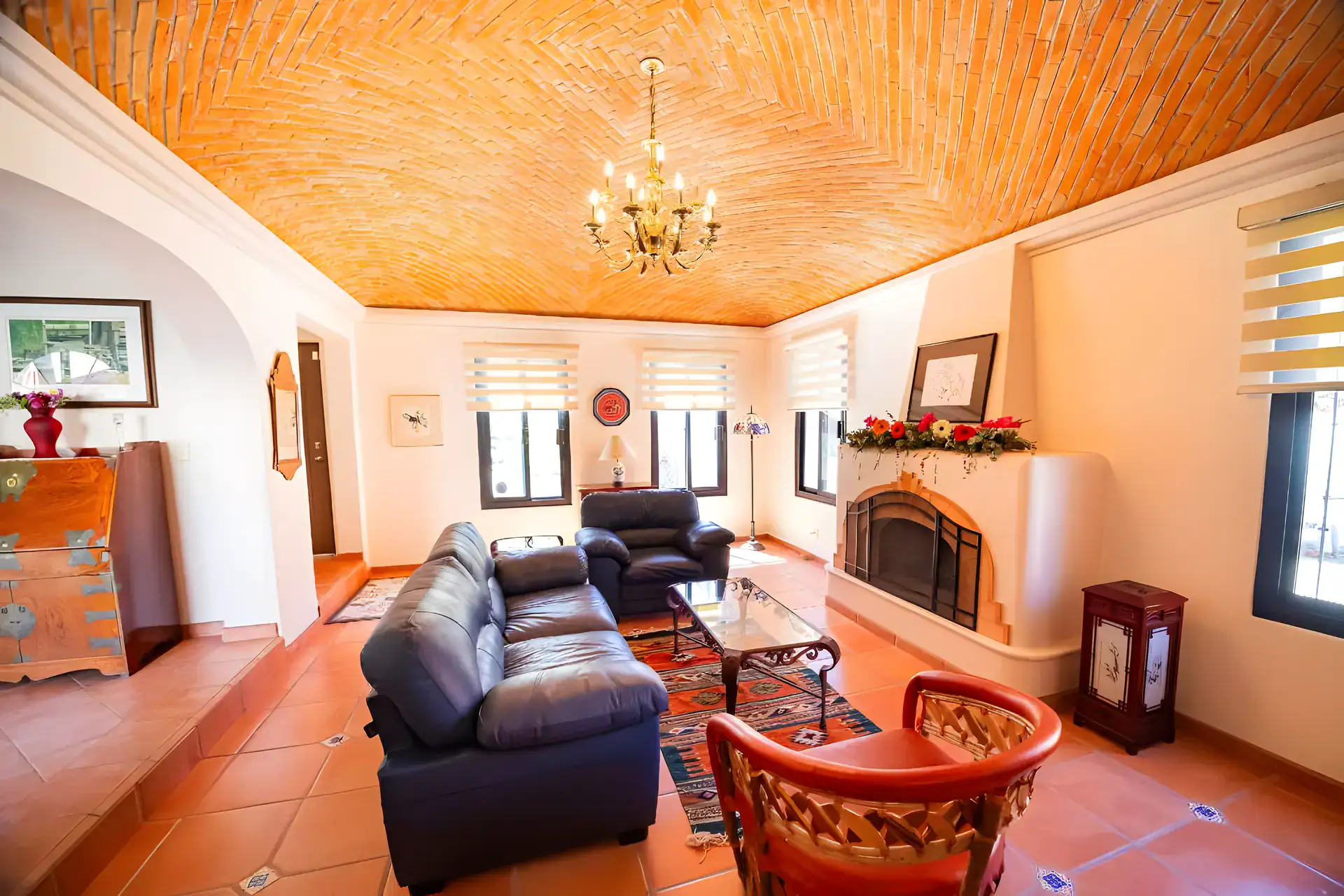 Casa Winston, living room with navy leather sofas, a fireplace with holiday garland and a brick vaulted ceiling with a chandelier, San Miguel de Allende