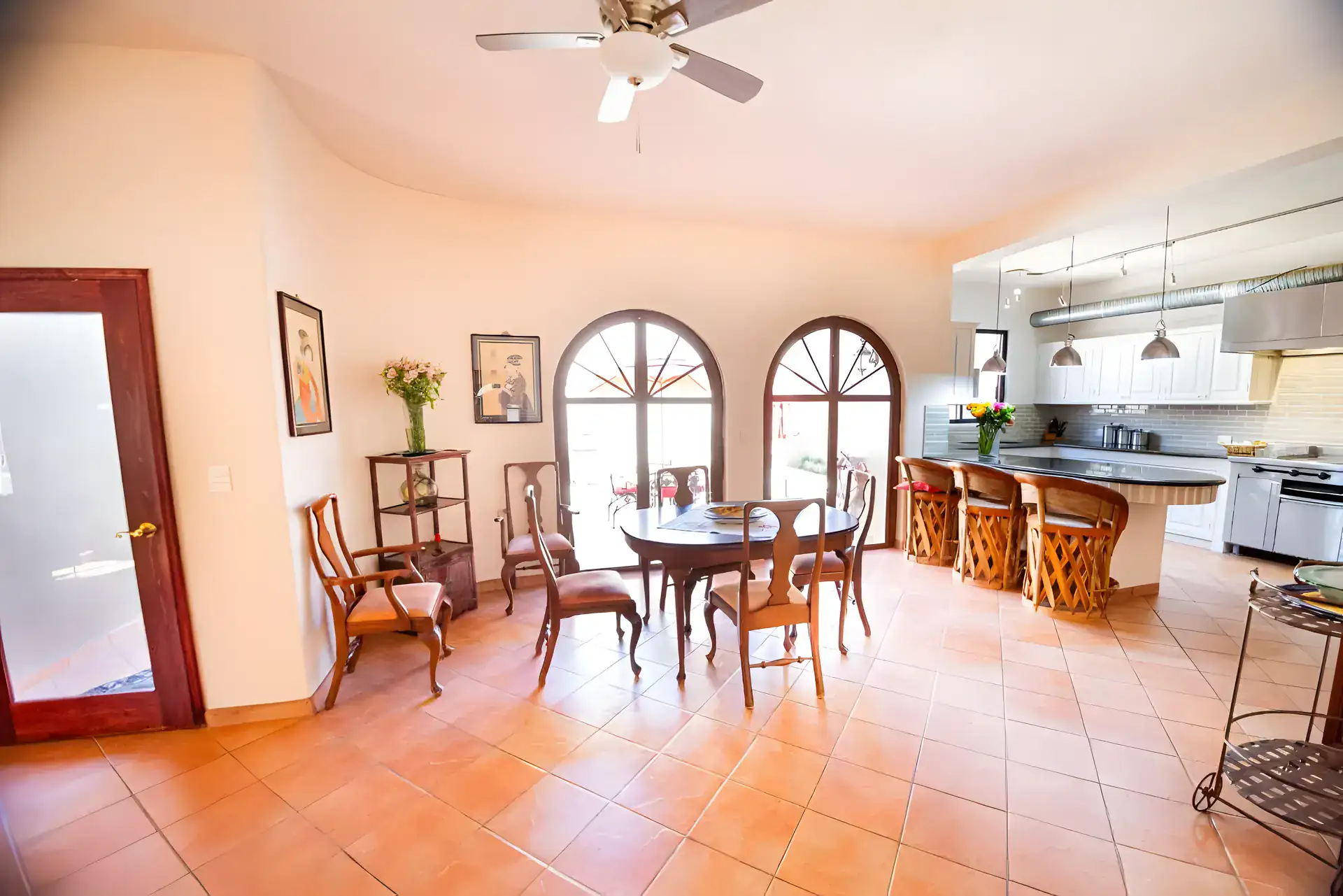 Casa Winston, dining area with an oval wood table, chairs, arched windows and an open kitchen with an island and bar stools, San Miguel de Allende