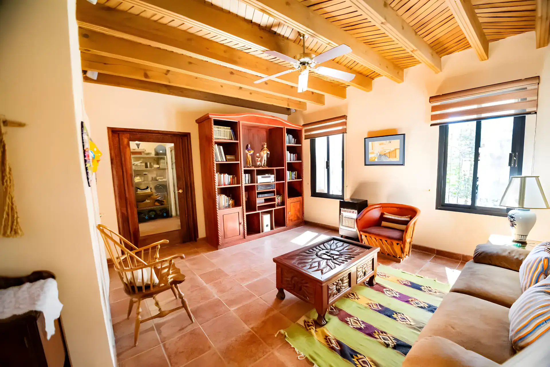 Casa Winston, family room with a wood beam ceiling, a tan sofa, a carved wood coffee table, a bookcase and a leather chair, San Miguel de Allende