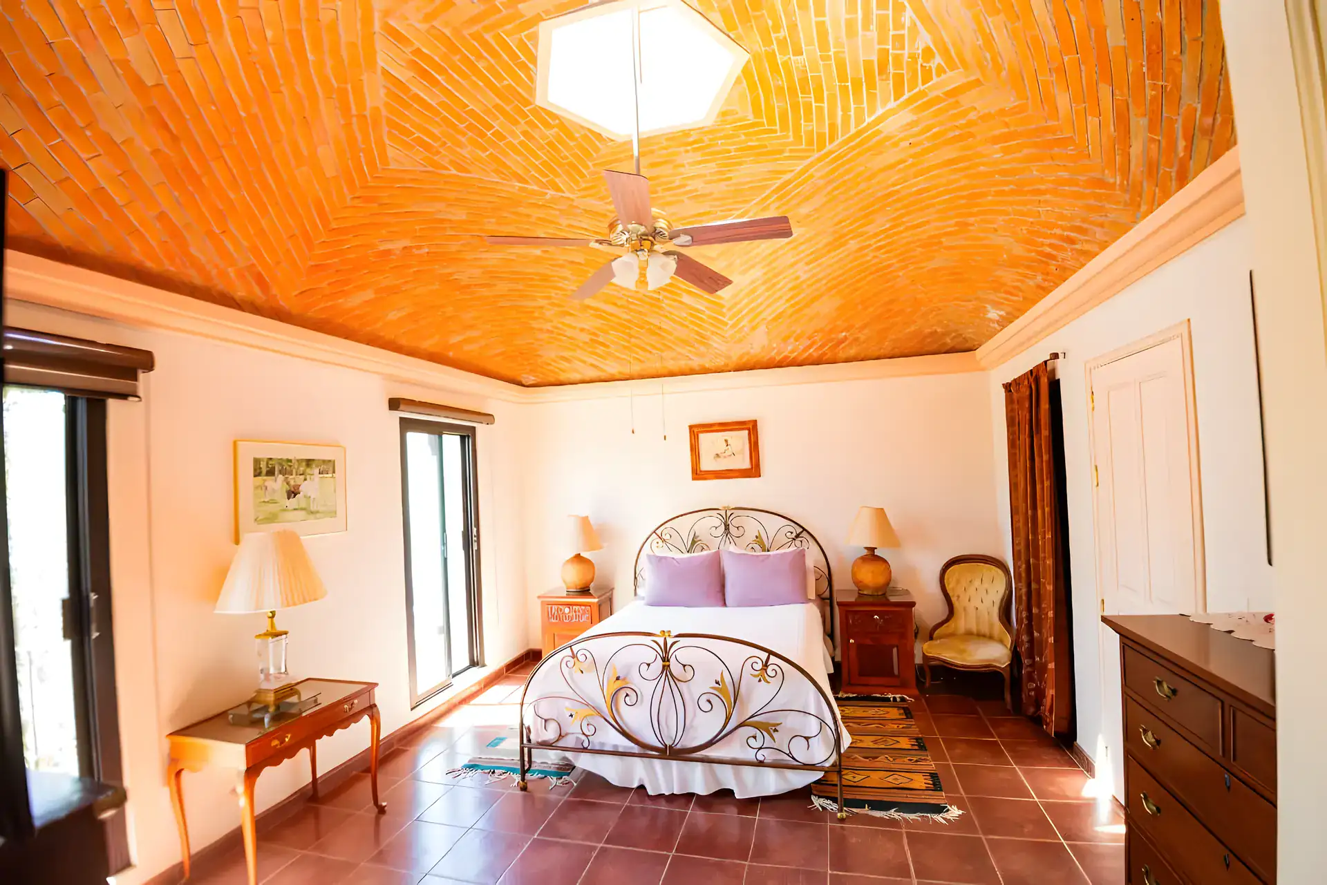 Casa Winston, bedroom with a brick vaulted ceiling, an iron bed with purple pillows, French doors and a ceiling fan, San Miguel de Allende