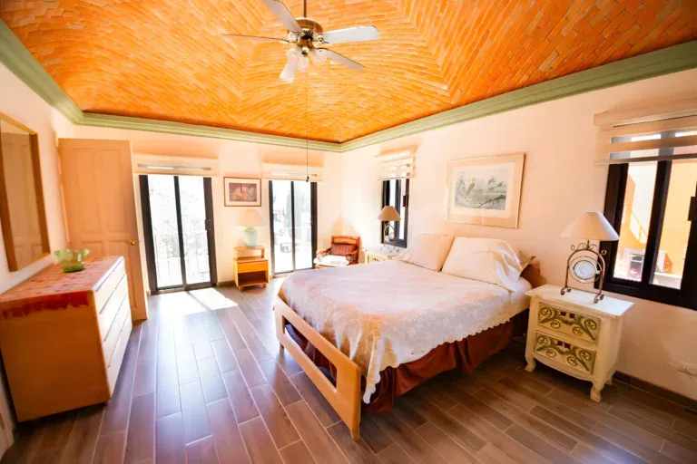 Casa Winston, bedroom with a brick vaulted ceiling, a wood bed with a lace spread and a sliding glass door to a balcony, San Miguel de Allende