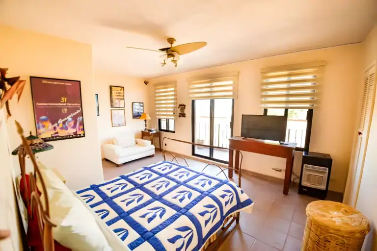Casa Winston, bedroom with a blue and white quilt, an iron bed, a wood desk, a television and balcony doors, San Miguel de Allende