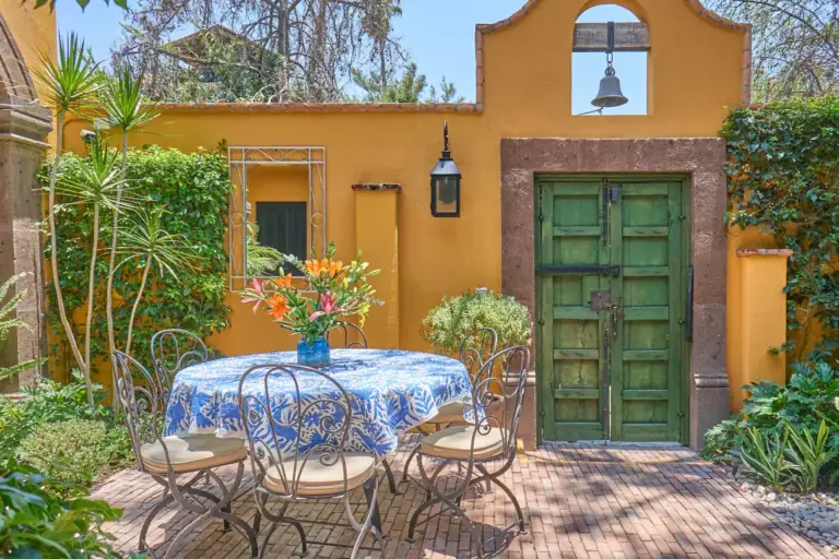 Casa Zaca, courtyard with a blue tablecloth dining set and a green door in a yellow wall, San Miguel de Allende