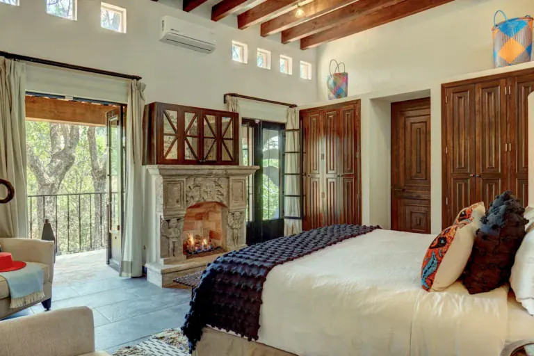Casa Zaca, bedroom with a stone fireplace, a bed with dark throws and terrace doors, San Miguel de Allende