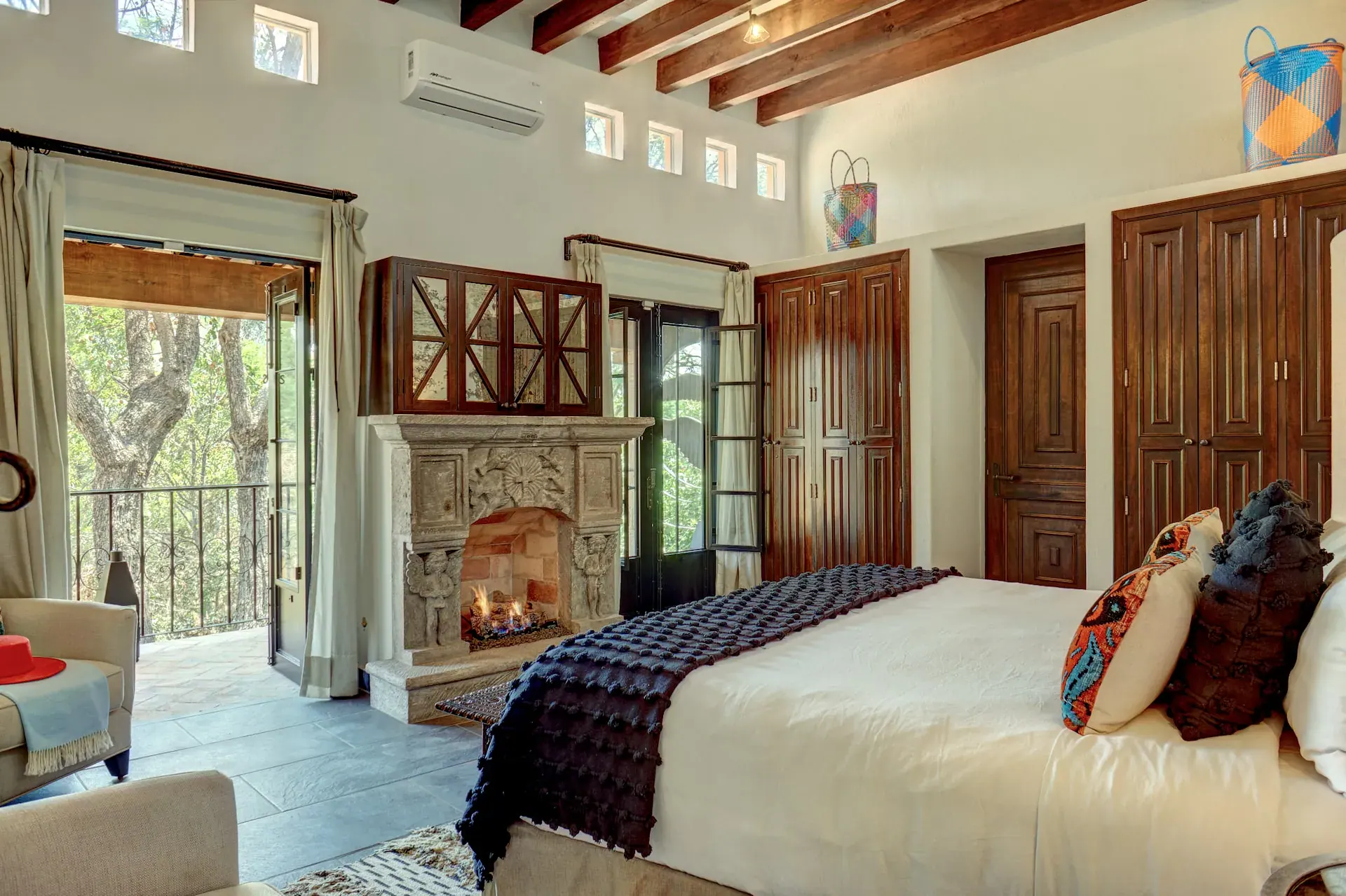 Casa Zaca, bedroom with a stone fireplace, a bed with dark throws and terrace doors, San Miguel de Allende