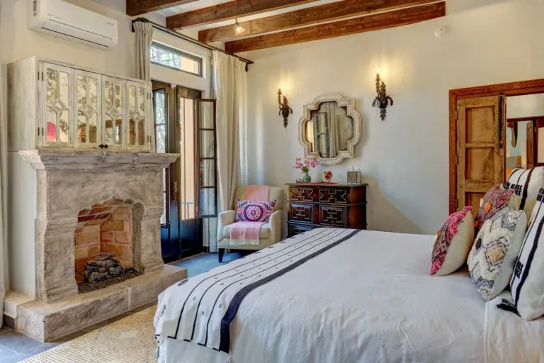 Casa Zaca, bedroom with a stone fireplace, a vanity and striped bedding, San Miguel de Allende