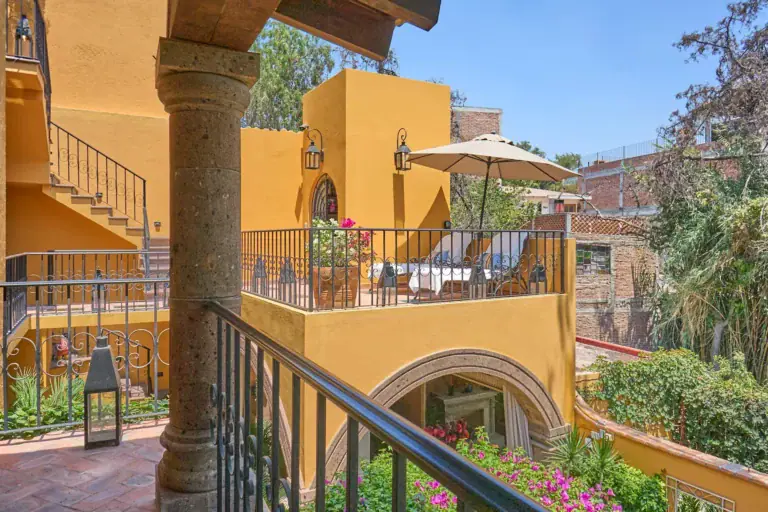 Casa Zaca, balcony above the courtyard with a yellow stairway and a patio umbrella, San Miguel de Allende