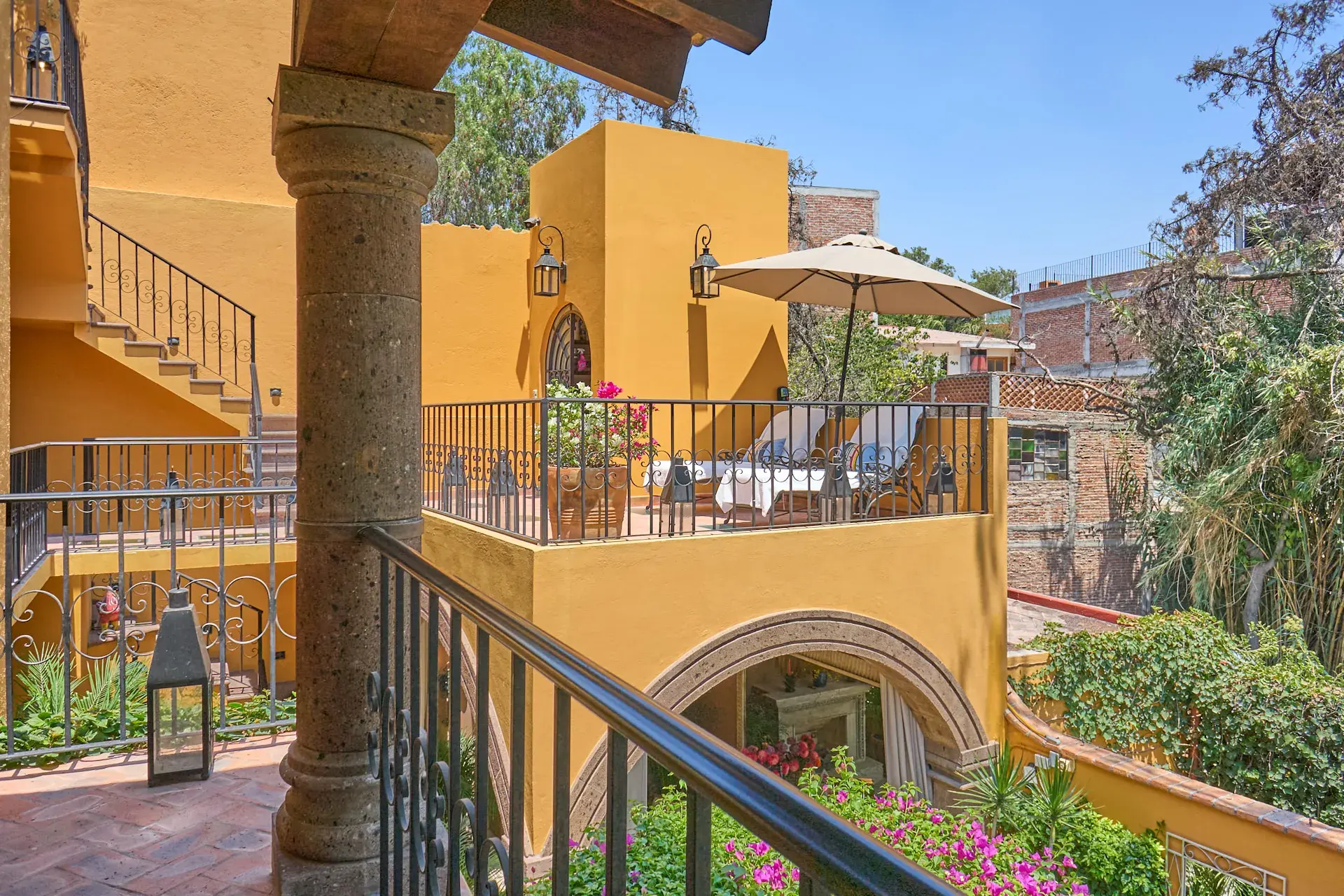 Casa Zaca, balcony above the courtyard with a yellow stairway and a patio umbrella, San Miguel de Allende
