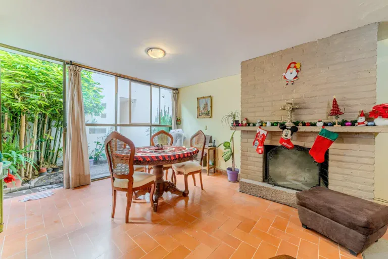 Casitas Terraplen, dining table with cane-back chairs beside a brick fireplace with Christmas stockings and a glass wall to the garden, San Miguel de Allende