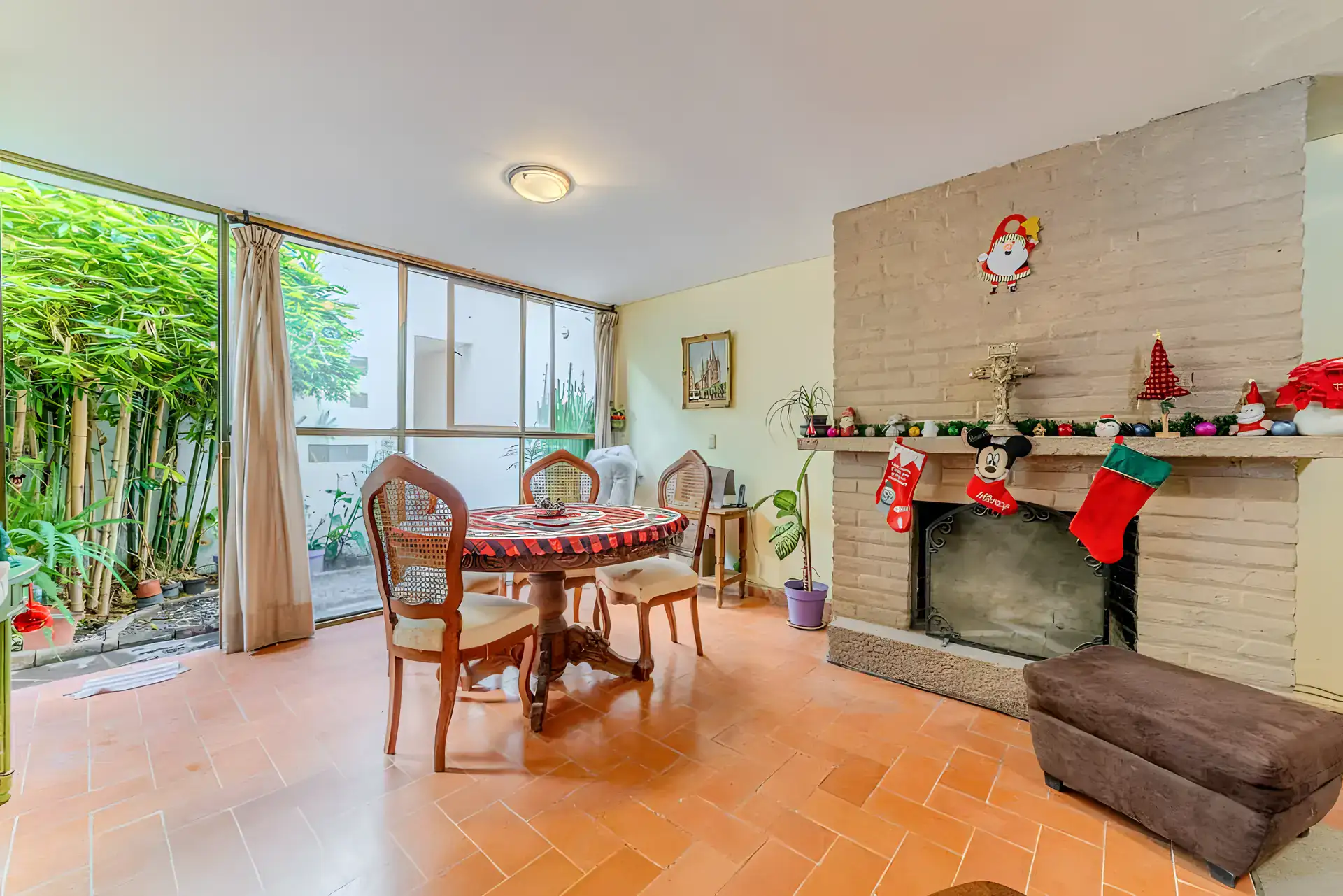 Casitas Terraplen, dining table with cane-back chairs beside a brick fireplace with Christmas stockings and a glass wall to the garden, San Miguel de Allende