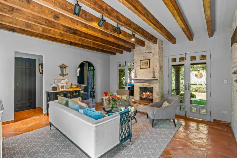 Cuesta de San Jose 22, living room with a white sofa, gray armchairs, a stone fireplace and French doors to the garden under a heavy timber beam ceiling, San Miguel de Allende