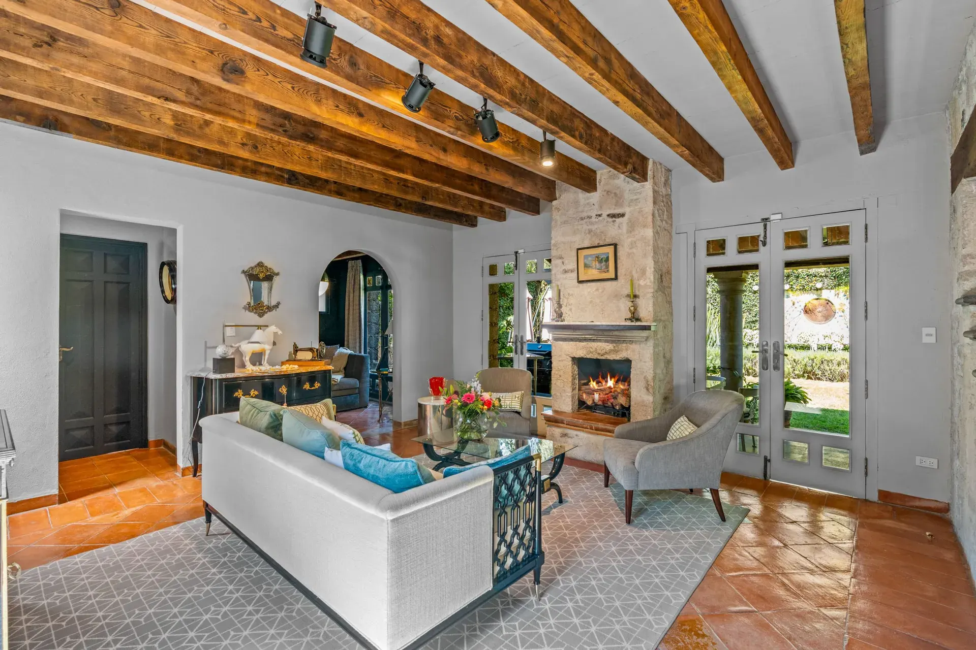 Cuesta de San Jose 22, living room with a white sofa, gray armchairs, a stone fireplace and French doors to the garden under a heavy timber beam ceiling, San Miguel de Allende