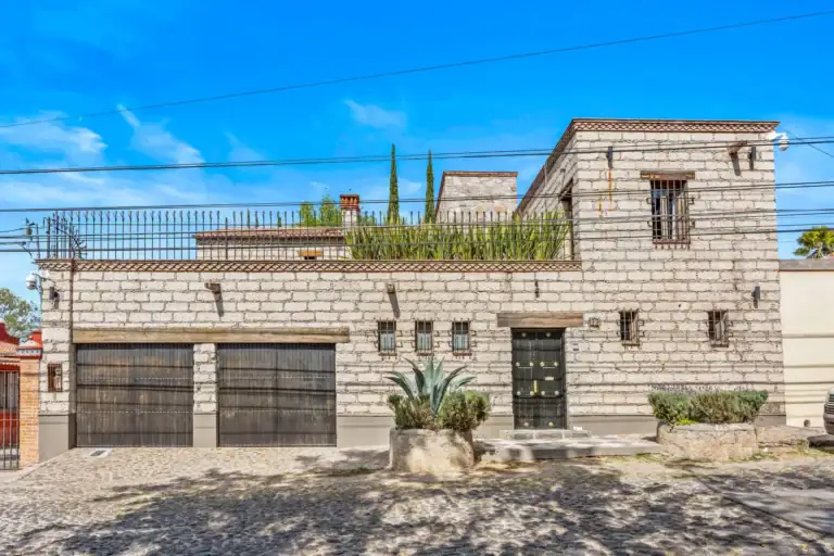 Cuesta de San Jose 22, stone facade of the house with two dark garage doors, barred windows, an agave and a cobblestone street, San Miguel de Allende