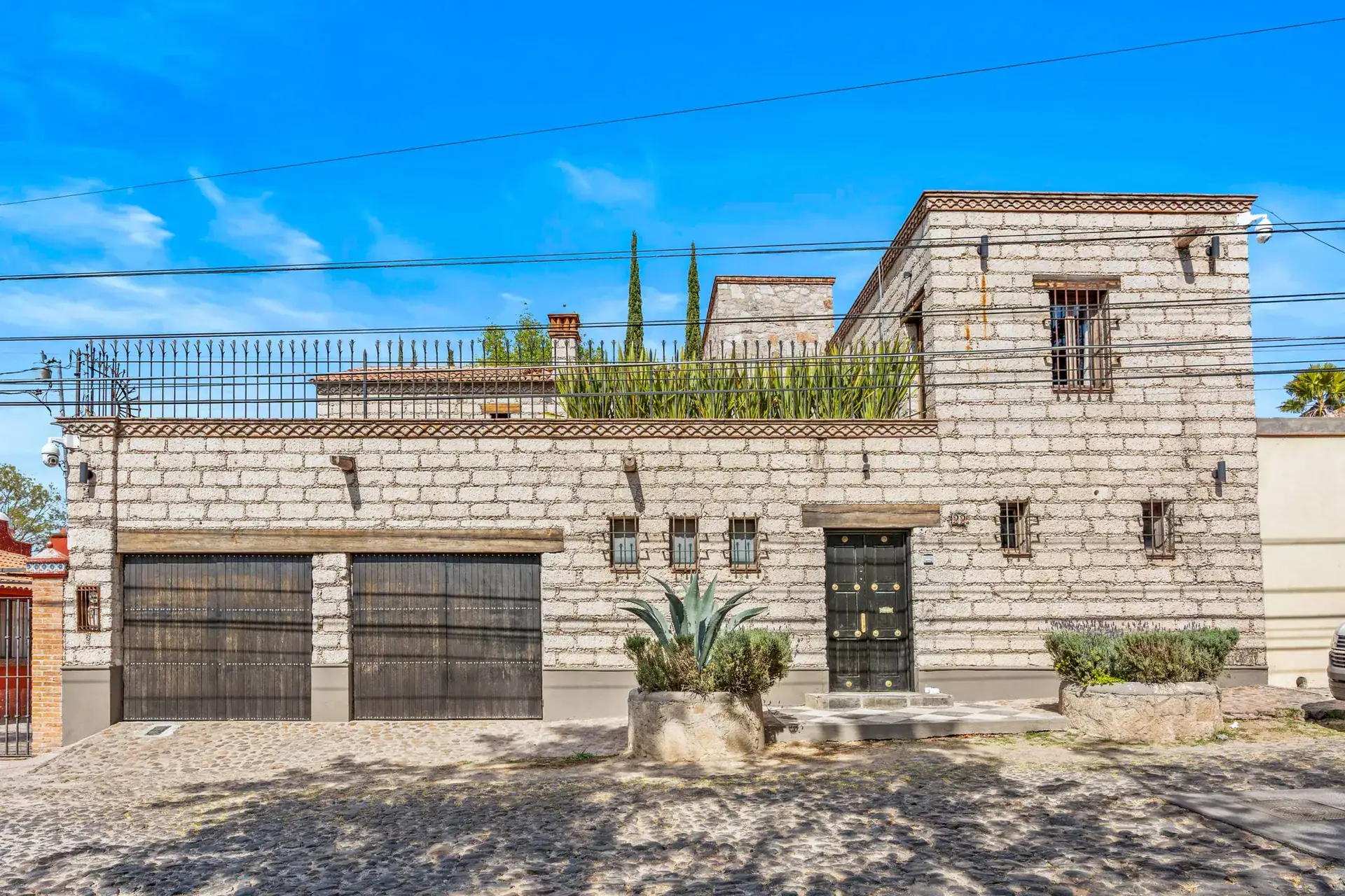Cuesta de San Jose 22, stone facade of the house with two dark garage doors, barred windows, an agave and a cobblestone street, San Miguel de Allende