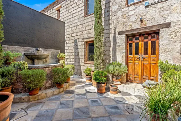 Cuesta de San Jose 22, entry courtyard with a stone wall fountain, potted shrubs, a checkered stone floor and a wooden double door, San Miguel de Allende