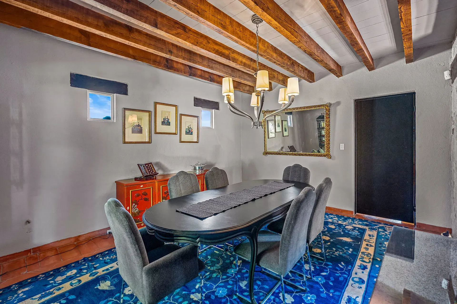 Cuesta de San Jose 22, dining room with a black oval table, gray upholstered chairs and a chandelier beneath timber beams, San Miguel de Allende