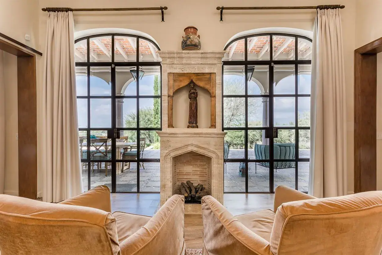 Finca Garambullos, sitting room with a stone fireplace framed by arched glass doors, San Miguel de Allende