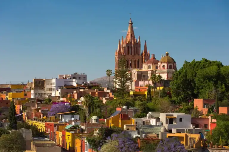 Hillside view of colorful San Miguel de Allende homes with the Parroquia spire rising above jacaranda trees