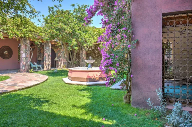 Hacienda Candelaria, courtyard fountain on a lawn beside a pink wall and flowering vines, San Miguel de Allende
