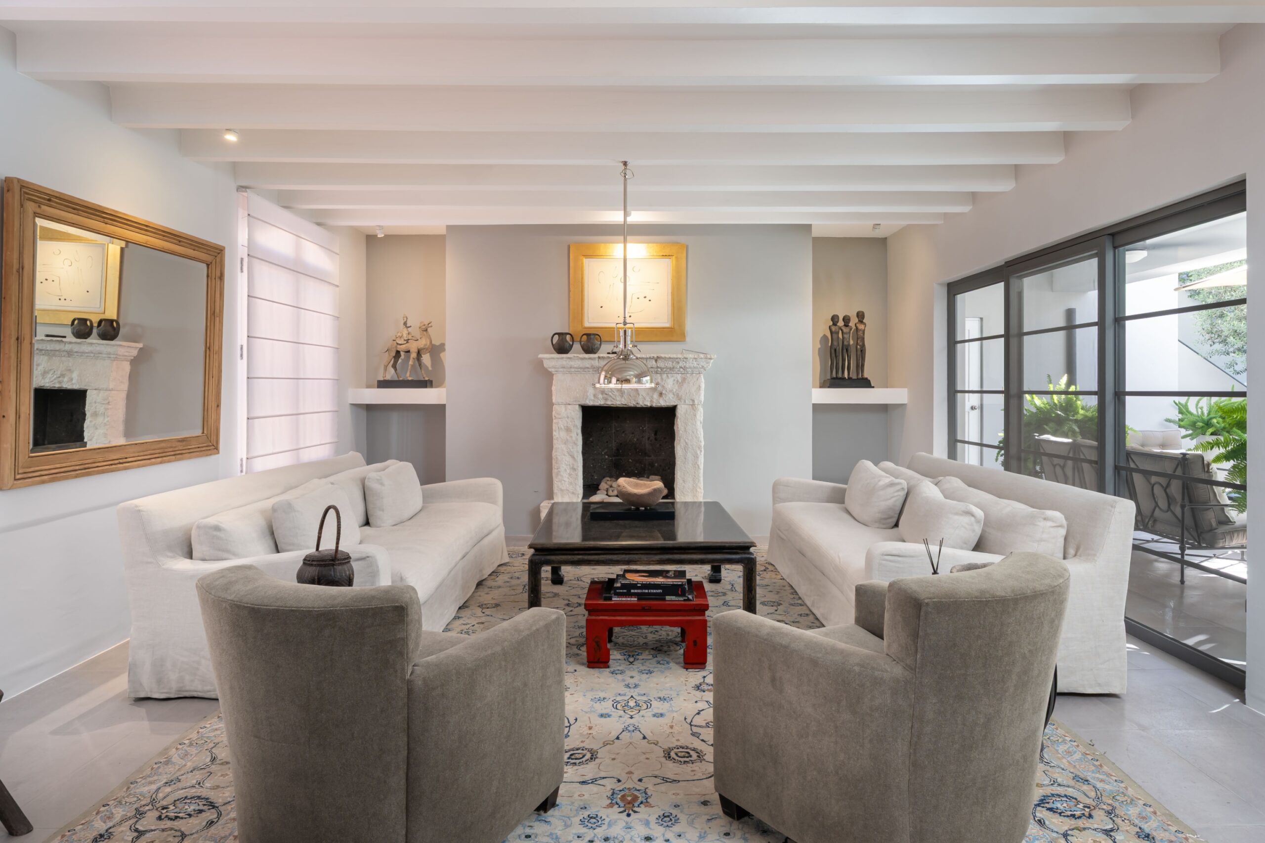 Open living room with a white beamed ceiling, gray walls, and a stone fireplace centered between built-in shelves and decor, San Miguel de Allende