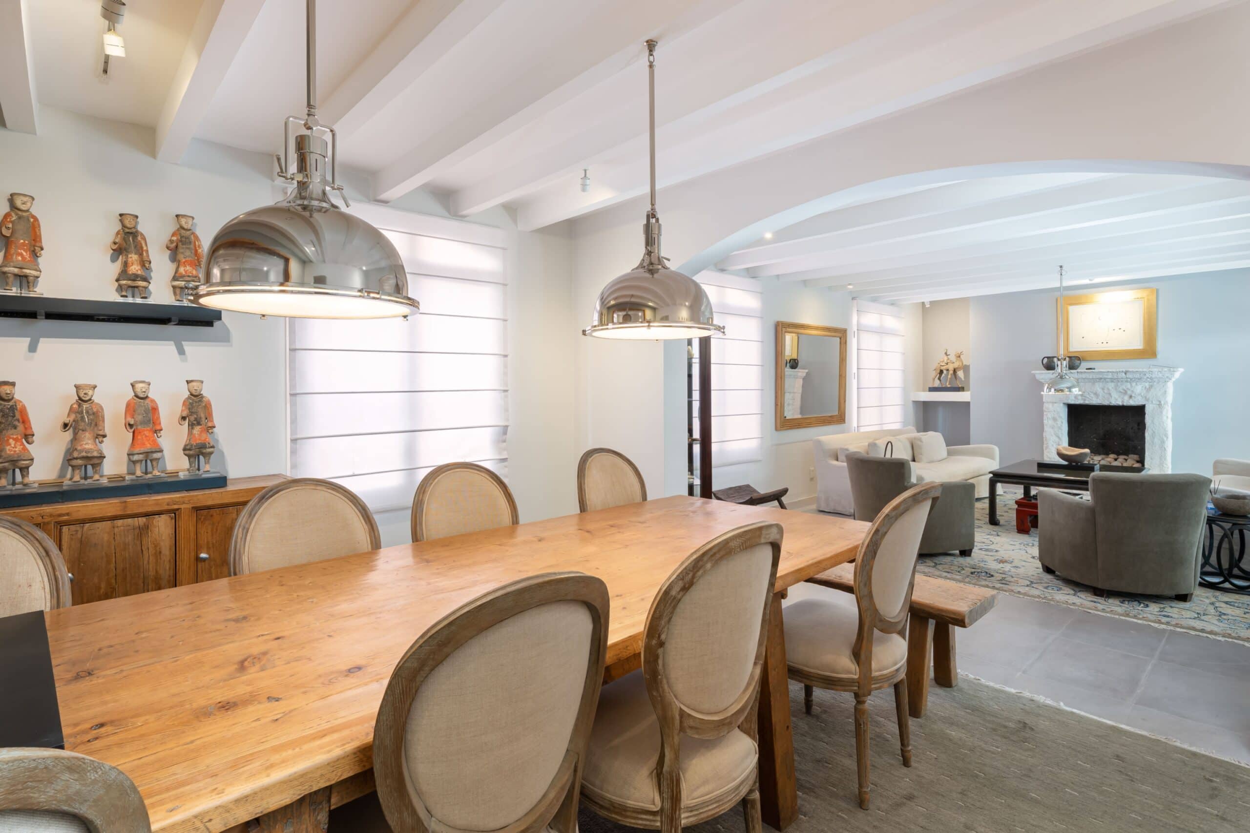 Bright dining room with a long wooden table, beige upholstered chairs, and large chrome pendant lights overhead in a light-filled space, San Miguel de Allende